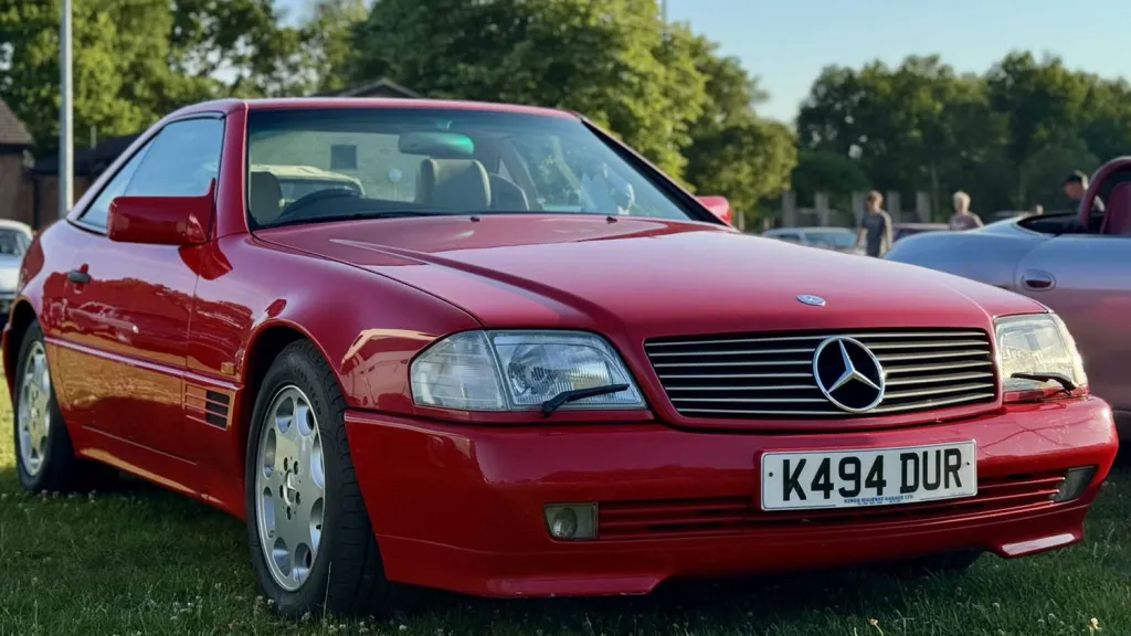Front view of red Mercedes-Benz SL R129 convertible parked on grass at outdoor event